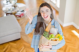 Beautiful young woman holding paper bag full of healthy groceries very happy and excited, winner expression celebrating victory