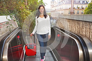 Beautiful woman with suitcase going up escalator