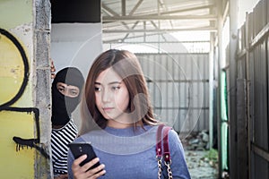 Beautiful young woman holding smartphone and being stalked by man criminal with the knife