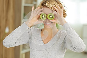 Beautiful young woman holding two kiwis on eyes