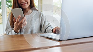 A young woman holding and using mobile phone with laptop computer on wooden table