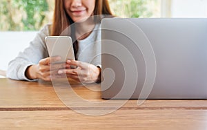 A young woman holding and using mobile phone with laptop computer on wooden table