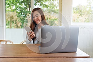A young woman holding and using mobile phone with laptop computer on wooden table