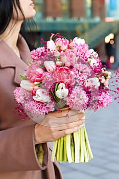 Beautiful young woman holding bridal bouquet in pink lilac tones made of hyacinth, tulips and gypsophila