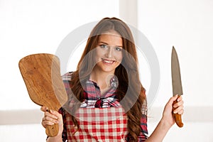 Beautiful young woman holding wooden bord and knife in kitchen