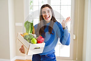 Beautiful young woman holding wooden box full of healthy groceries very happy and excited, winner expression celebrating victory