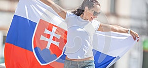 Krásna mladá žena drží vlajku Slovenska vonku za slnečného dňa v slnečných okuliaroch