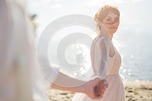 A beautiful young woman,holds the hand of the man in the open air. Follow me. The haze is created for romantic frame.