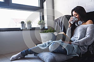 Beautiful young woman at home drinking coffee reading a book