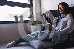 Beautiful young woman at home drinking coffee reading a book