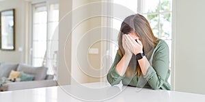 Beautiful young woman at home with sad expression covering face with hands while crying