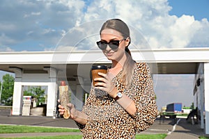 Beautiful young woman with hot dog and coffee at gas station