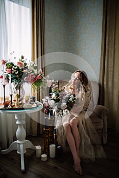 Beautiful young woman in a house dress in the boudoir, decorated with beautiful flowers, sitting on a white bed with a canopy, fas