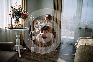 Beautiful young woman in a house dress in the boudoir, decorated with beautiful flowers, sitting on a white bed with a canopy, fas