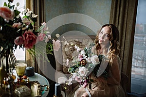 Beautiful young woman in a house dress in the boudoir, decorated with beautiful flowers, sitting on a white bed with a canopy, fas