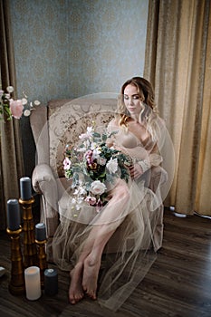 Beautiful young woman in a house dress in the boudoir, decorated with beautiful flowers, sitting on a white bed with a canopy, fas