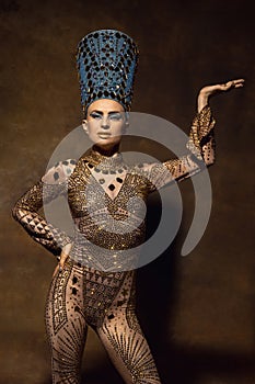 Beautiful young woman in image of Nefertiti in art performance  on brown vintage background. Retro style