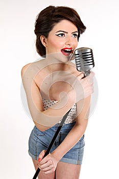 Beautiful young woman isolated on white in studio in old fashion clothes representing pinup and retro style with microphone