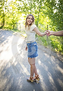 Beautiful young woman in a jean skirt holding her boyfriend`s hand and looking back