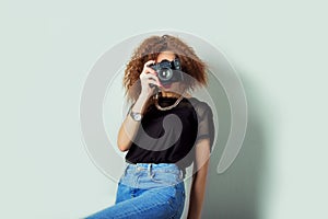 Beautiful young woman in jeans with a camera in the hands of curly hair in the Studio