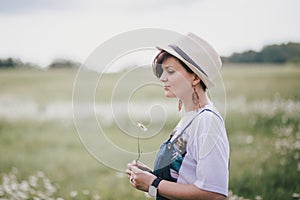 Beautiful young woman in a jeans dress and straw hat posing in a camomile field