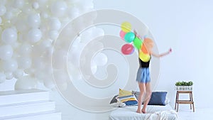 Beautiful young woman jumping on the bed with balloons