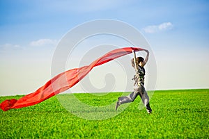 Beautiful young woman jumping on a green meadow with colored tissue