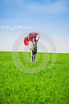 Beautiful young woman jumping on a green meadow with colored tissue