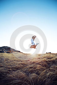 Beautiful young woman jumping on a meadow in the mountain
