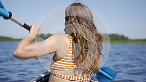 Beautiful young woman kayaking on lake. Girl rowing oars on a kayak on the river. Sports hike, water rafting in nature