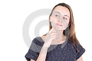 Beautiful young woman keeps finger on face looks aside with bewilderment poses against white background