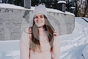 Beautiful young woman in knitted sweater in winter park. Cold weather outdoors. Snow Happy smiling portrait of girl