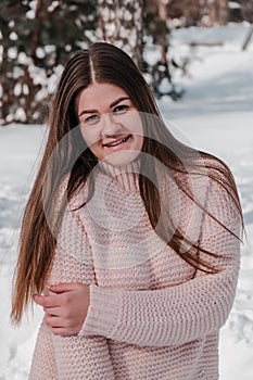 Beautiful young woman in knitted sweater in winter park. Cold weather outdoors. Snow Happy smiling portrait of girl