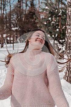 Beautiful young woman in knitted sweater in winter park. Cold weather outdoors. Snow Happy smiling portrait of girl