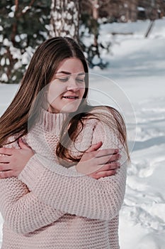 Beautiful young woman in knitted sweater in winter park. Cold weather outdoors. Snow Happy smiling portrait of girl