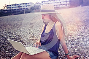Beautiful young woman with a laptop on the beach at sunset