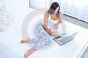 Beautiful young woman with laptop in bed