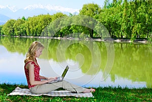 Beautiful young woman with laptop near the lake