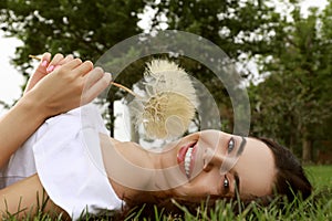 Beautiful young woman with large dandelion lying on green grass in park. Allergy free concept