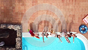 Beautiful young woman lay down enjoying and relaxing on an inflatable ice cream lilo in a blue clear swimming pool - holiday