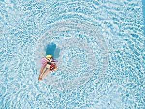 Beautiful young woman lay down enjoying and relaxing on an inflatable ice cream lilo in a blue clear swimming pool - holiday