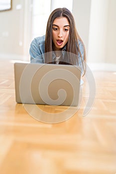 Beautiful young woman laying on the floor using laptop scared in shock with a surprise face, afraid and excited with fear