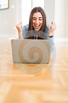 Beautiful young woman laying on the floor using laptop screaming proud and celebrating victory and success very excited, cheering