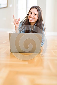 Beautiful young woman laying on the floor using laptop very happy pointing with hand and finger to the side