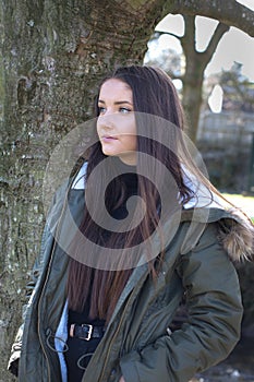 Beautiful young woman leaning against a tree