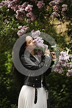 Beautiful young woman in leather jacket enjoying the smell of the bloomy lilac tree in springtime photo