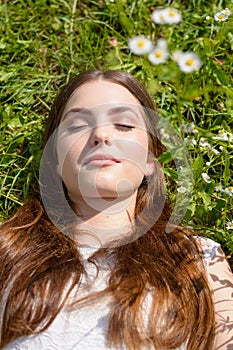 Beautiful young woman lies with her eyes closed on a flower meadow