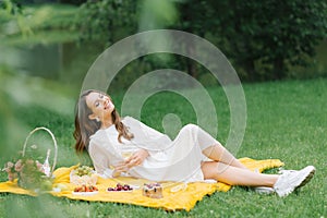 A beautiful young woman lies on a yellow blanket on the grass, holding a glass of wine