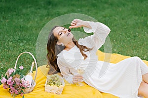 A beautiful young woman lies on a yellow blanket on the grass, holding a glass of wine