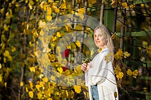 Beautiful young woman with light brown hair in a white sweater on a background of foliage in an autumn park.